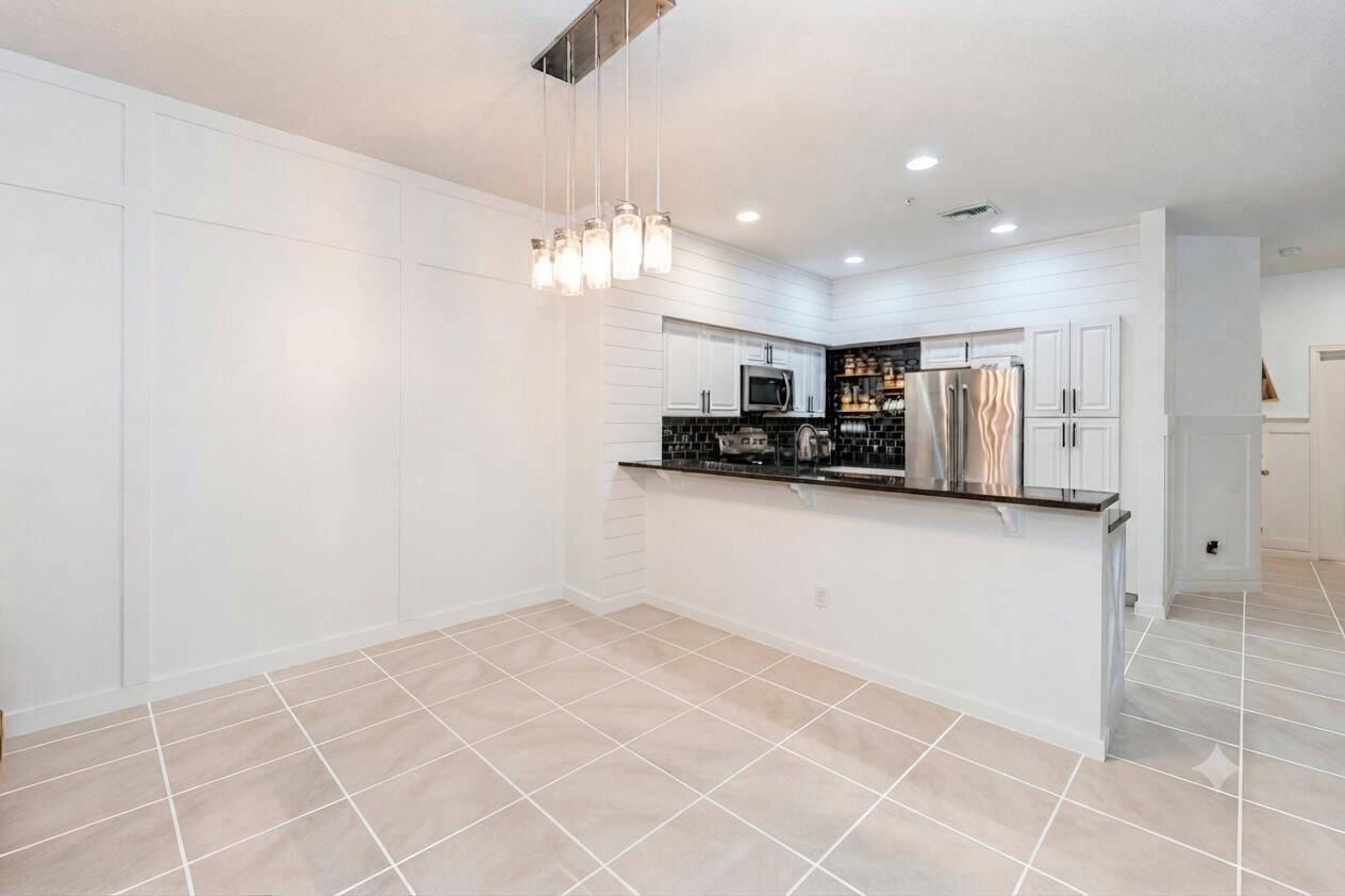 A kitchen with white cabinets, a breakfast bar, and a dining area with pendant lighting — 4466 Leo Lane, Riviera Beach FL 33410, RIVIERA BEACH, FL