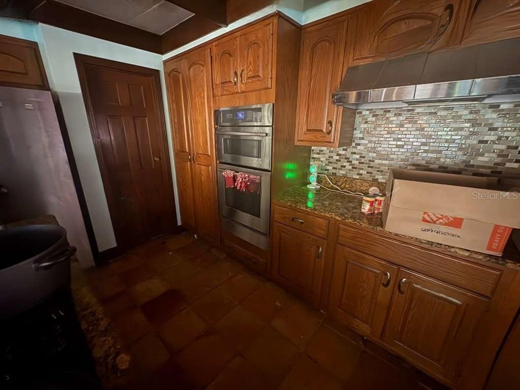 A kitchen features wood cabinets, stainless steel double ovens, a tiled backsplash, and granite countertops — 122 FAIRWAY DRIVE, HAINES CITY, FL