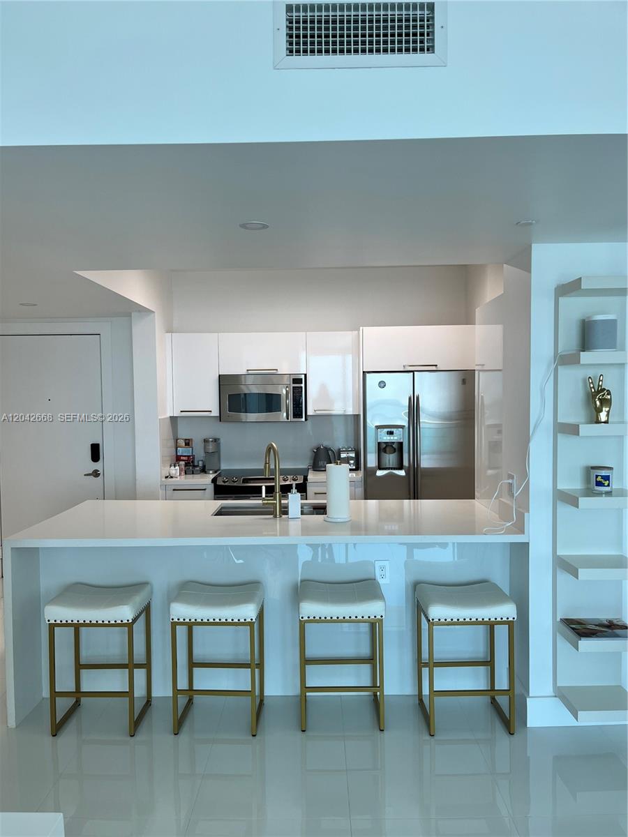 A modern kitchen features white cabinetry, stainless steel appliances, and a breakfast bar with stools — 951 Brickell Ave # 2704, Miami FL 33131, MIAMI, FL