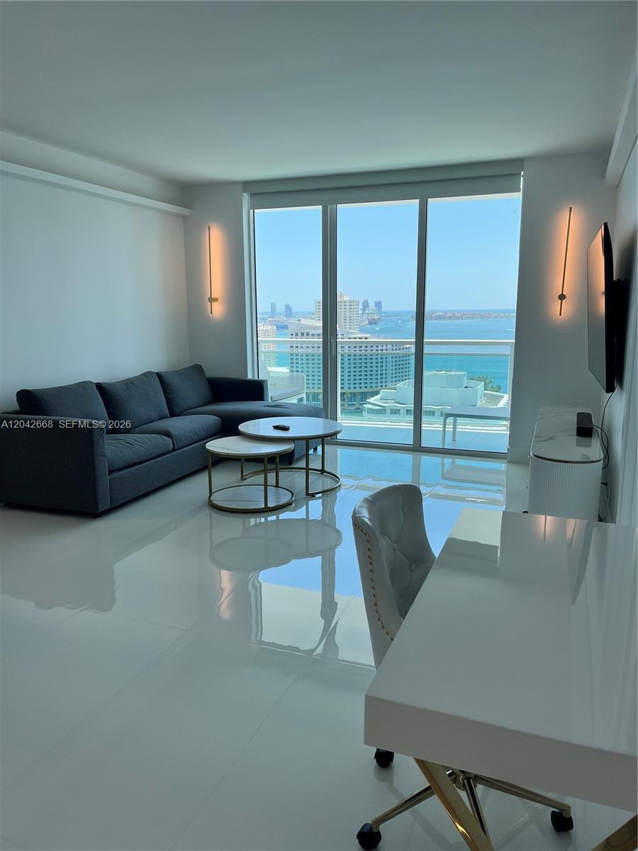 A modern living room features a dark sofa, nested coffee tables, and a balcony view — 951 Brickell Ave # 2704, Miami FL 33131, MIAMI, FL