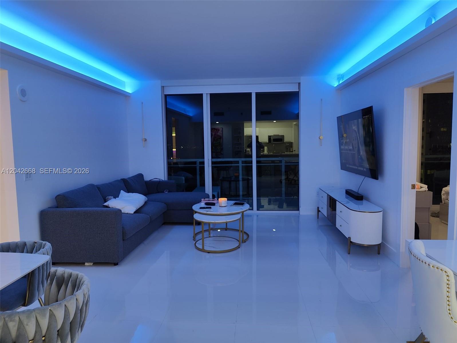 A living room features a blue sectional sofa, nested coffee tables, and blue ceiling lighting — 951 Brickell Ave # 2704, Miami FL 33131, MIAMI, FL
