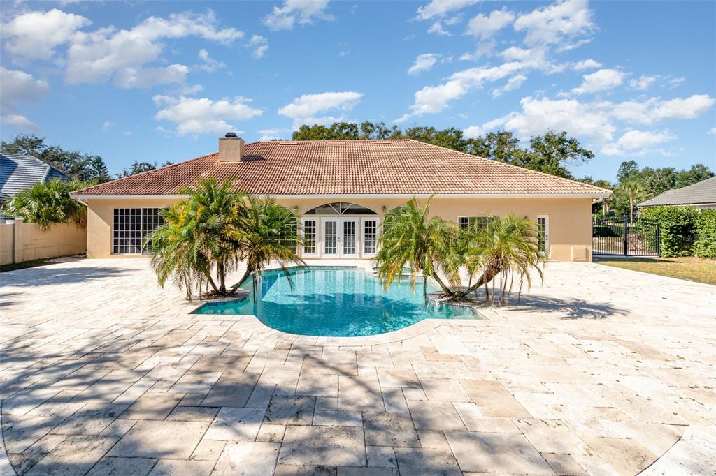 A backyard features a swimming pool surrounded by a large stone patio and palm trees — 9217 RIDGE PINE TRAIL, ORLANDO, FL