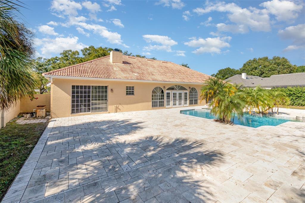 A tan house exterior features a large stone patio and a swimming pool in the backyard — 9217 RIDGE PINE TRAIL, ORLANDO, FL