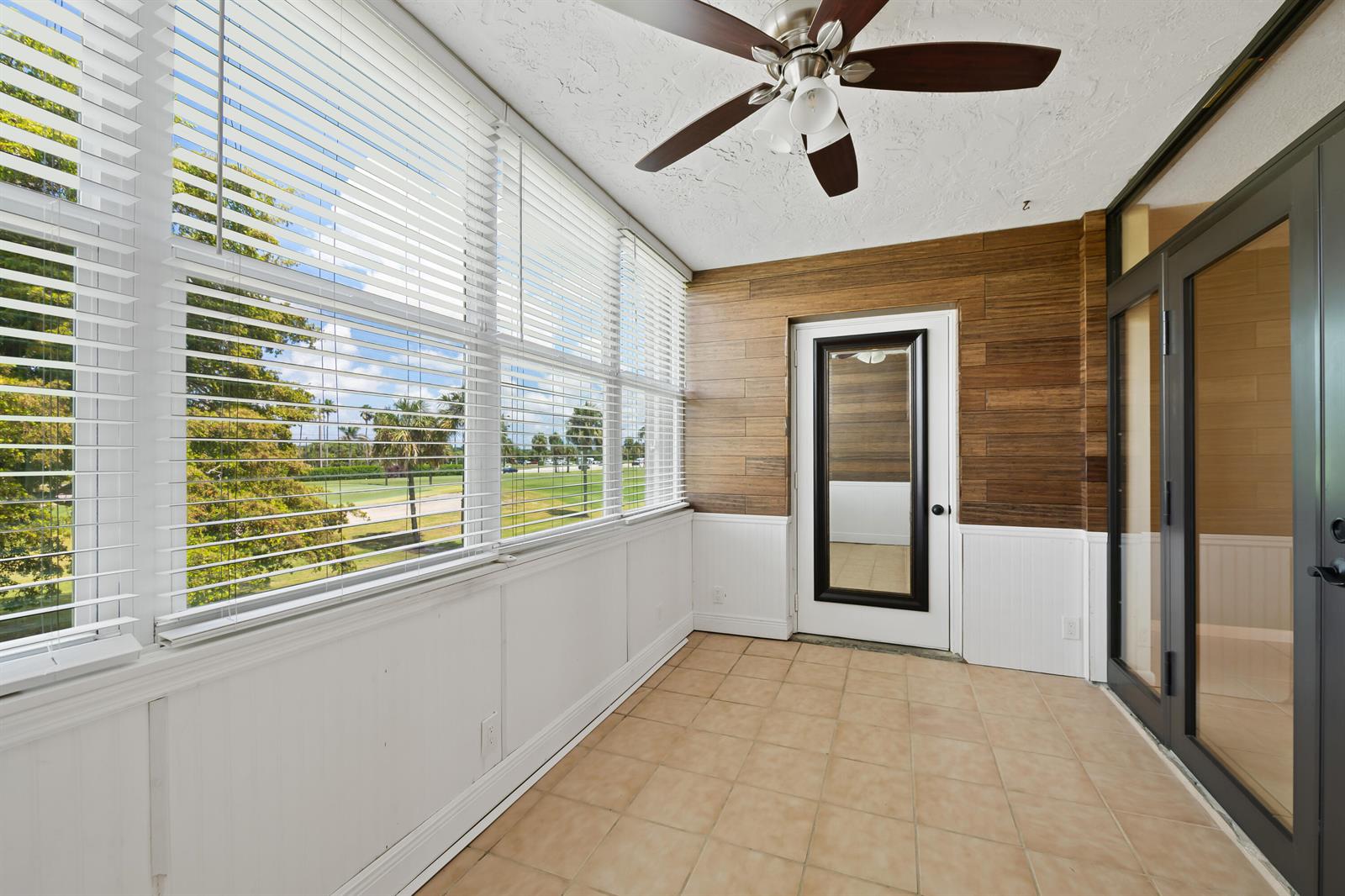 A sunroom with tile flooring, wood-paneled walls, a ceiling fan, and large windows overlooking greenery — 7350 NW 18th Street # 207, Margate FL 33063, MARGATE, FL