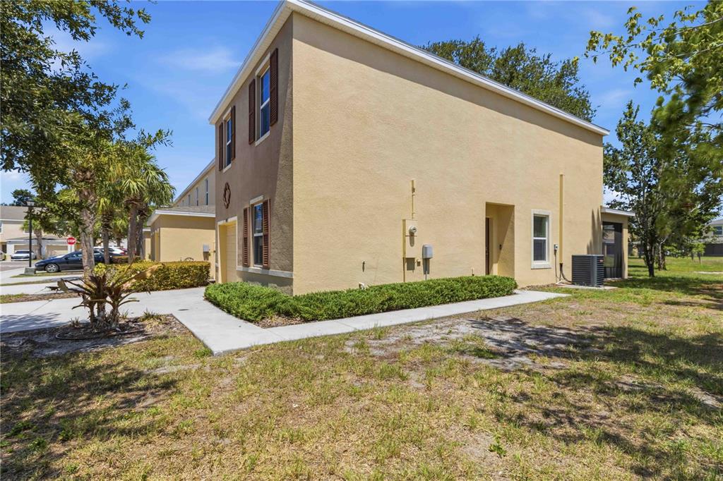 The exterior side view of a two-story tan stucco townhouse with a concrete walkway — 9973 HOUND CHASE DRIVE, GIBSONTON, FL