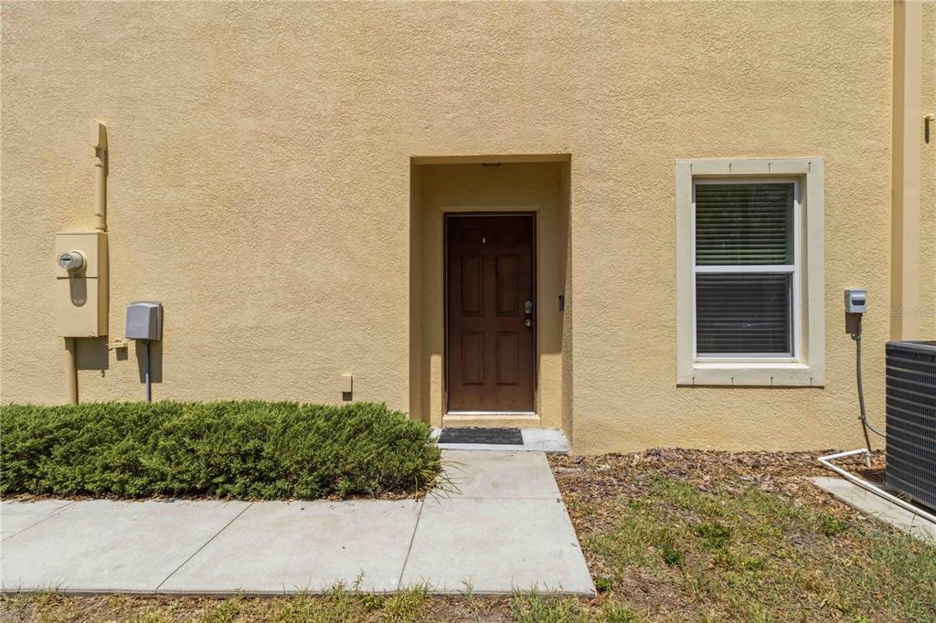The exterior of a tan stucco building features a brown front door and a window — 9973 HOUND CHASE DRIVE, GIBSONTON, FL