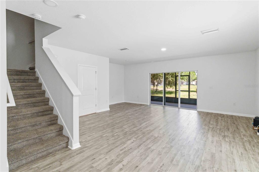 A bright living room features light wood-look flooring, white walls, and a carpeted staircase — 9973 HOUND CHASE DRIVE, GIBSONTON, FL