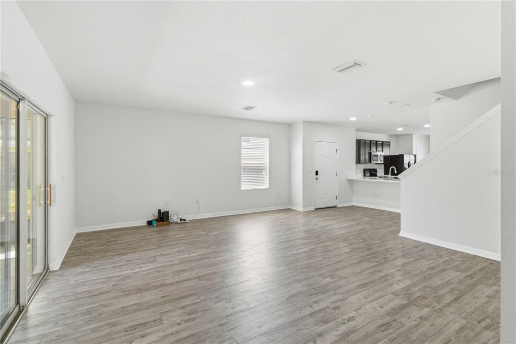 An open-concept living area features light wood-look flooring, white walls, a sliding glass door, and a kitchen — 9973 HOUND CHASE DRIVE, GIBSONTON, FL
