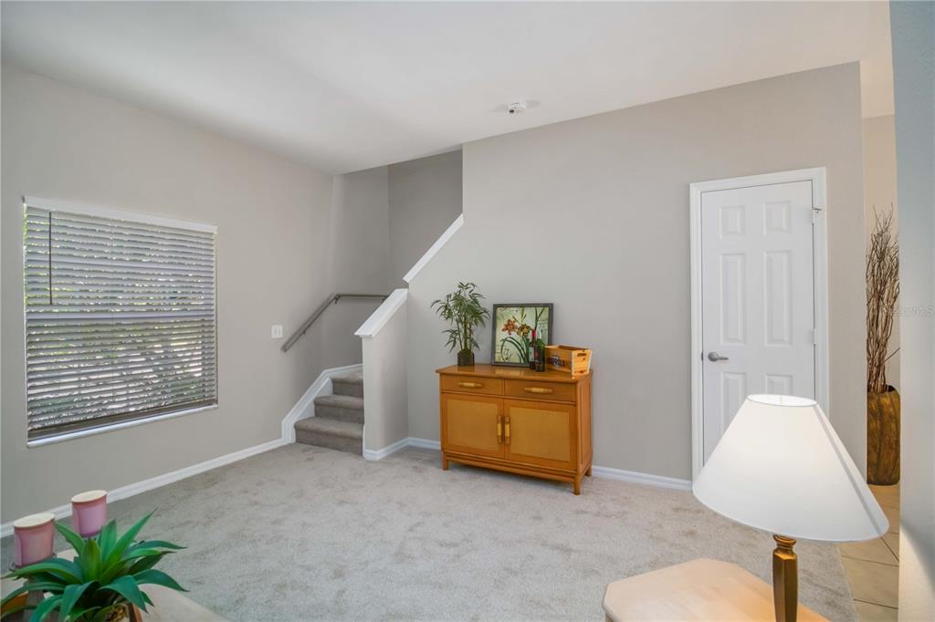 A carpeted living area features a wooden cabinet, a staircase, and a white interior door — 7794 PLANTATION CIRCLE, BRADENTON, FL