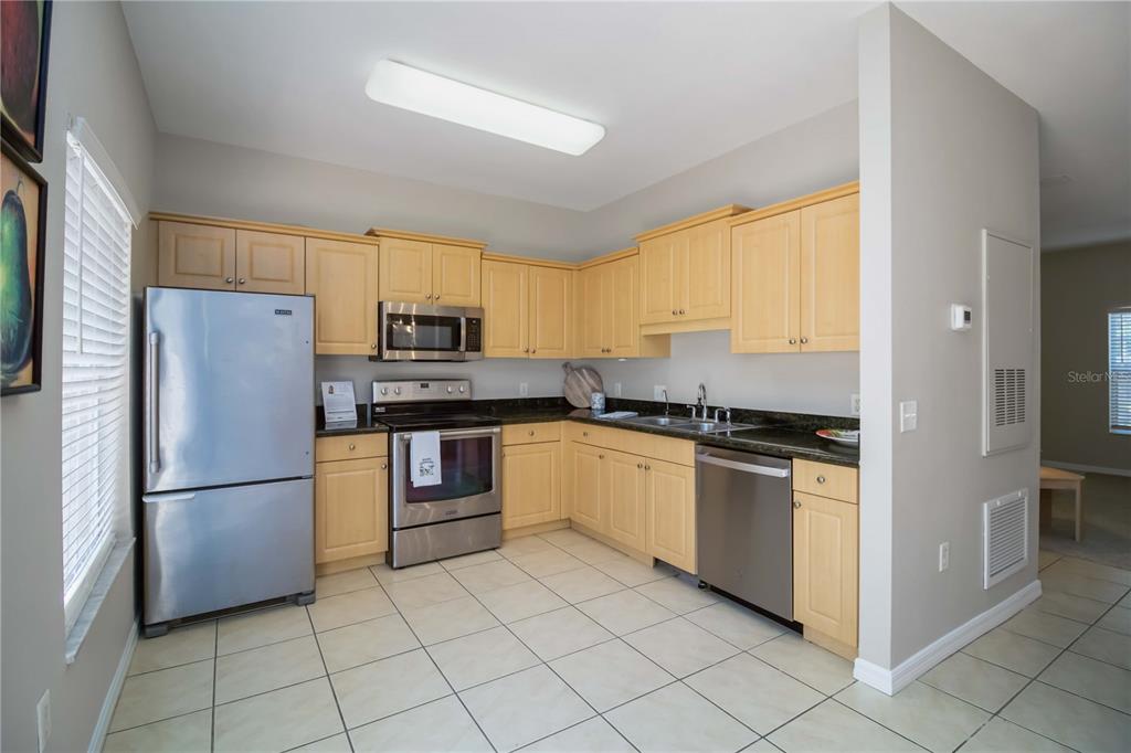 A kitchen features light wood cabinets, stainless steel appliances, dark countertops, and light tile flooring — 7794 PLANTATION CIRCLE, BRADENTON, FL