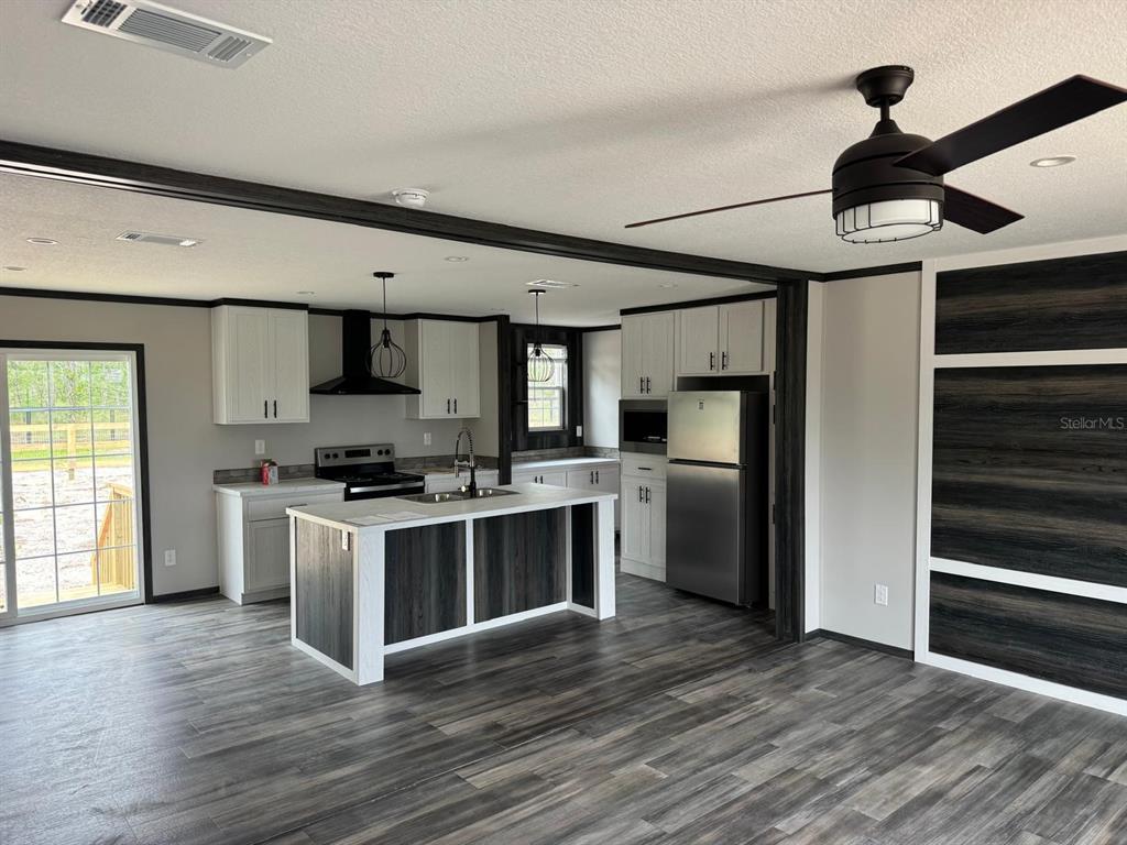 A modern kitchen features white cabinetry, a dark wood-paneled island, and stainless steel appliances — 14270 SE 60 STREET, MORRISTON, FL