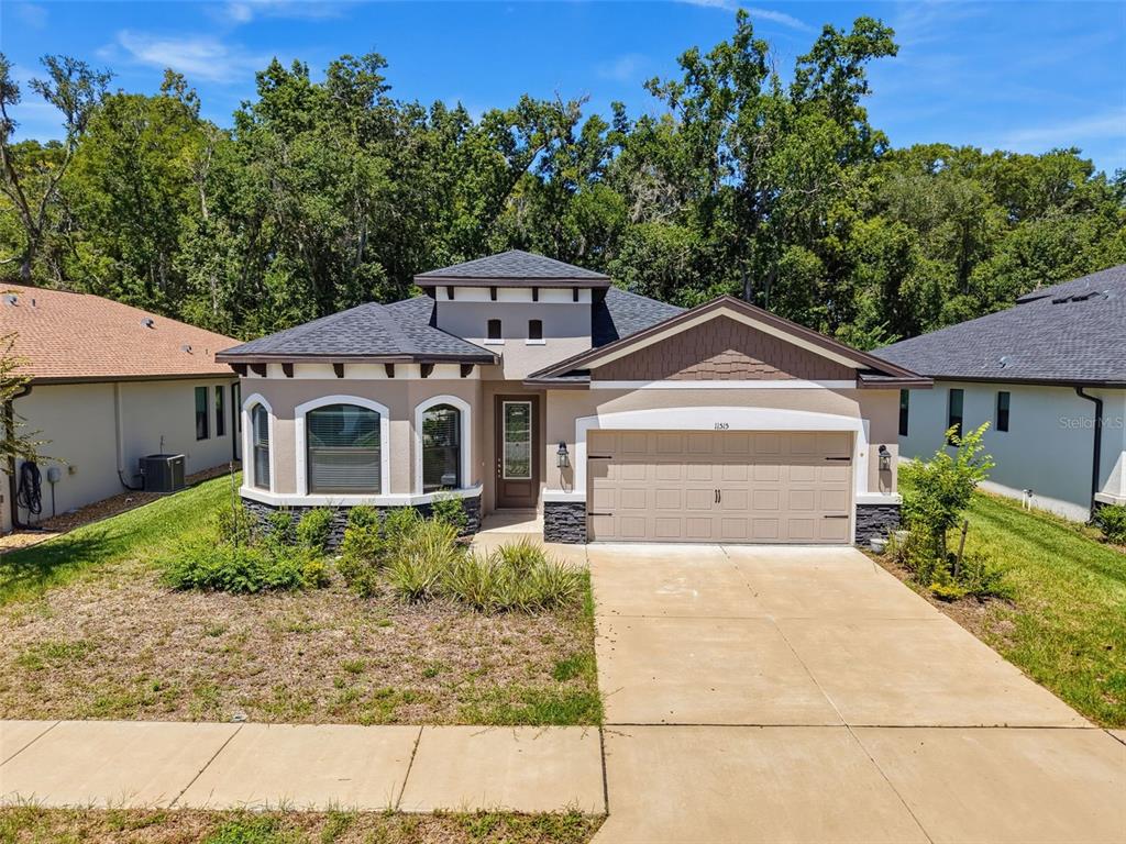 A single-story suburban house with a tan stucco exterior, dark roof, and two-car garage — 11515 WEAVER HOLLOW ROAD, NEW PORT RICHEY, FL