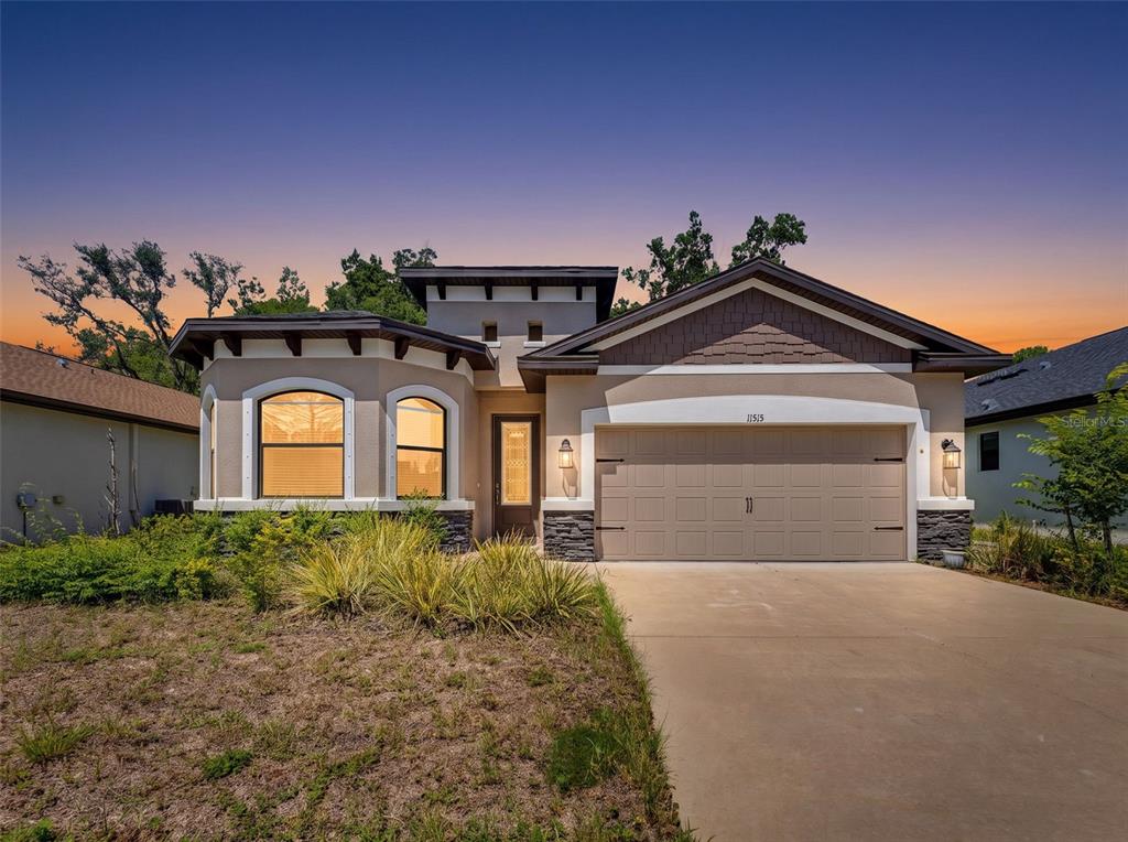 A single-story house with a beige stucco exterior, stone accents, and a two-car garage — 11515 WEAVER HOLLOW ROAD, NEW PORT RICHEY, FL
