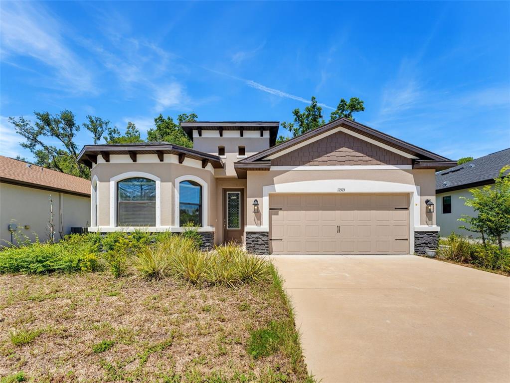 A single-story house with a beige stucco exterior, stone accents, and a two-car garage — 11515 WEAVER HOLLOW ROAD, NEW PORT RICHEY, FL