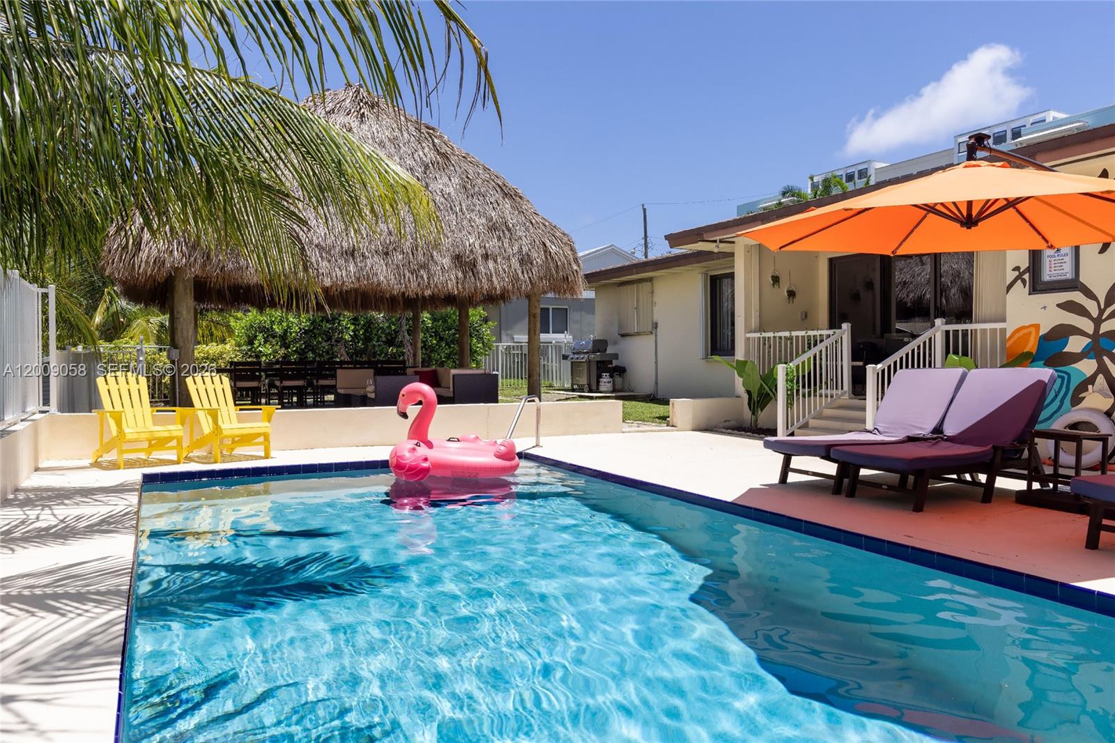 A swimming pool with a pink flamingo float sits in front of a thatched-roof gazebo — 155 SE 19th Ave # 0, Deerfield Beach FL 33441, DEERFIELD BEACH, FL
