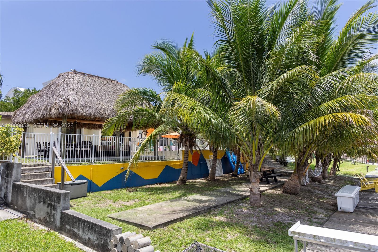 A thatched-roof structure sits above a yellow and blue retaining wall near palm trees — 155 SE 19th Ave # 0, Deerfield Beach FL 33441, DEERFIELD BEACH, FL