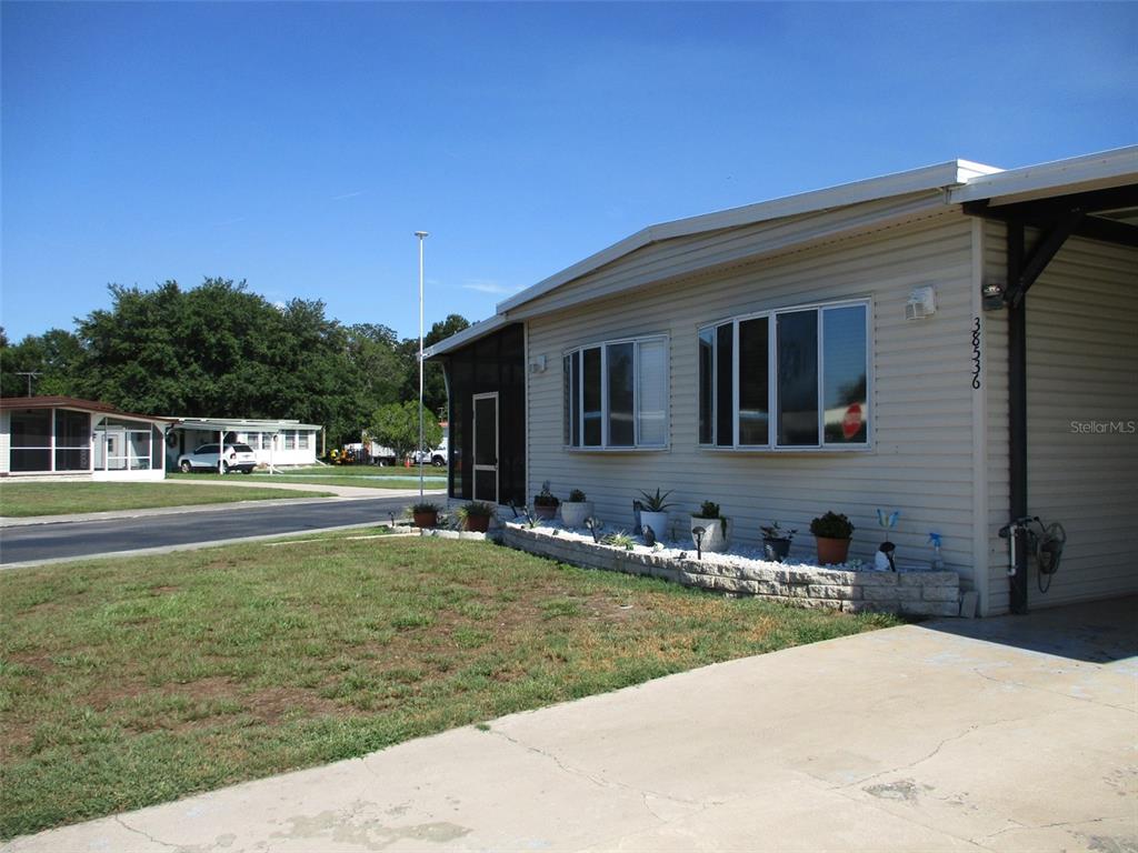 A beige mobile home with a carport, a stone planter, and a screened-in porch — 38536 CONE DRIVE, ZEPHYRHILLS, FL