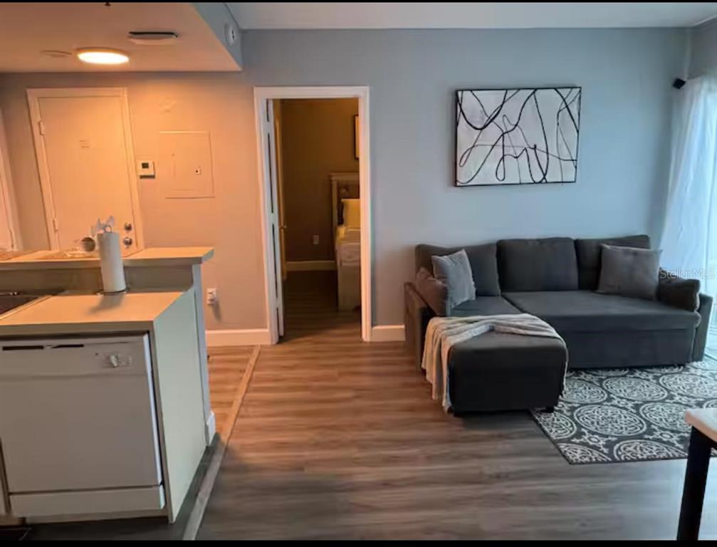 A living room with a gray sectional sofa, patterned rug, and an adjacent kitchen area — 6165 CARRIER DRIVE UNIT 3104, ORLANDO, FL