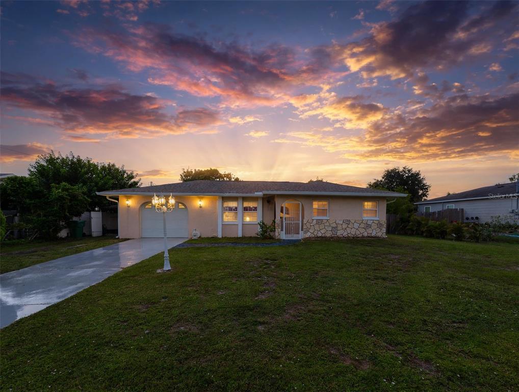 A single-story house with a stone facade, a garage, and a lawn at sunset — 451 READING STREET NW, PORT CHARLOTTE, FL