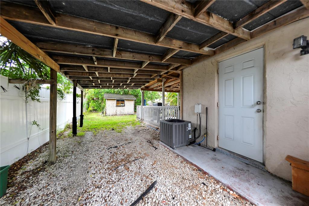A gravel-covered backyard area features a wooden patio cover, a white door, and an AC unit — 451 READING STREET NW, PORT CHARLOTTE, FL