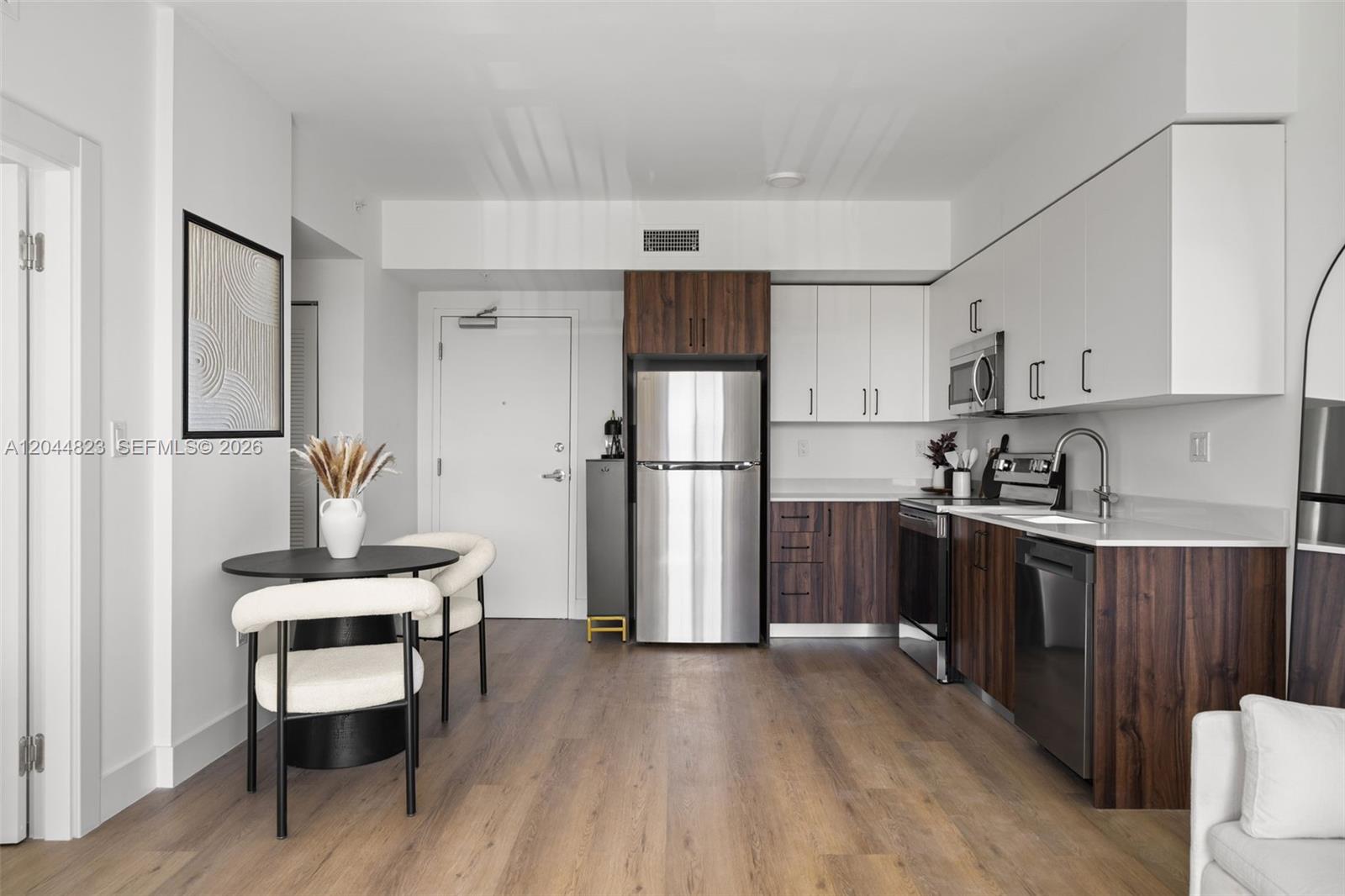 A kitchen and dining area feature white and wood cabinets, stainless appliances, and wood flooring — 2479 NE 192nd St # 207, Miami FL 33180, MIAMI, FL