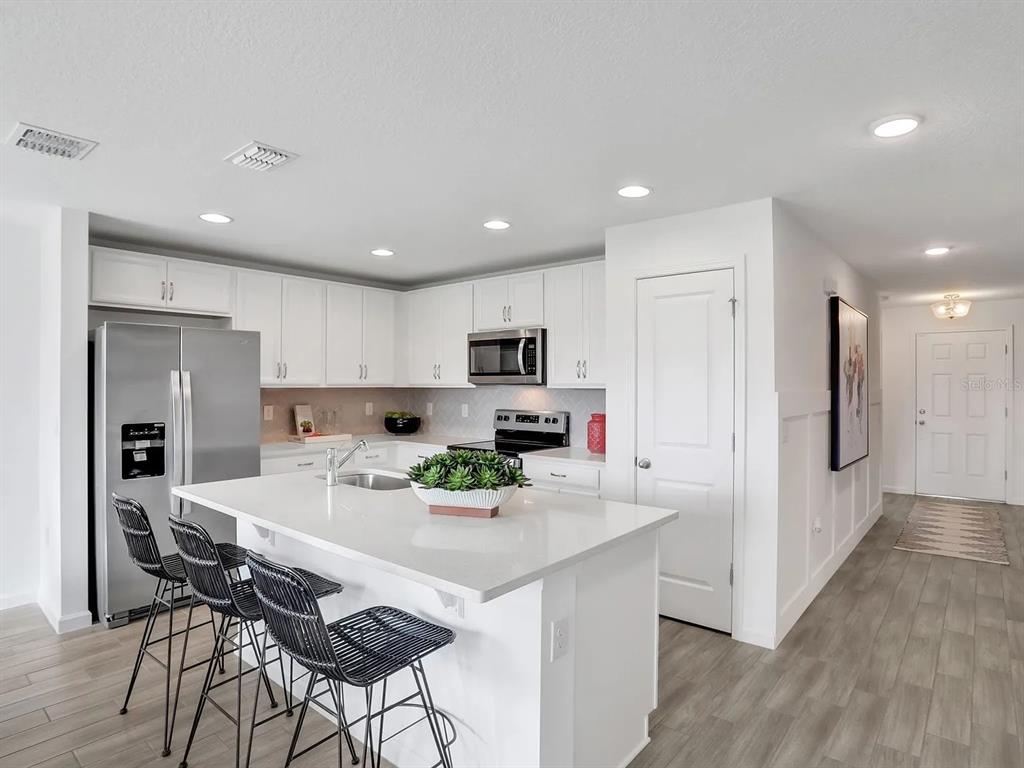 A modern kitchen features white cabinetry, a central island with bar seating, and stainless appliances — 123 BOTTLE BRUSH DRIVE, HAINES CITY, FL