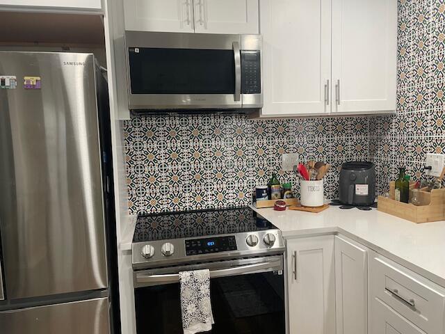 A kitchen features stainless steel appliances, white cabinetry, and a patterned tile backsplash — 31 Capri A # 31, Delray Beach FL 33484, DELRAY BEACH, FL