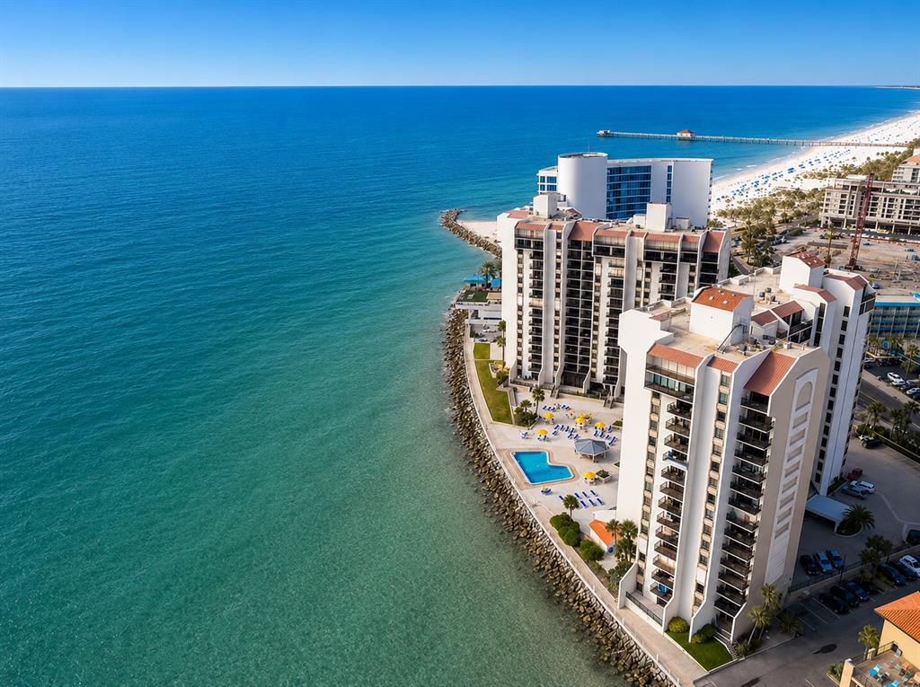 Aerial view of a coastal condominium complex with a swimming pool and rocky shoreline — 450 S GULFVIEW BOULEVARD UNIT 708, CLEARWATER BEACH, FL