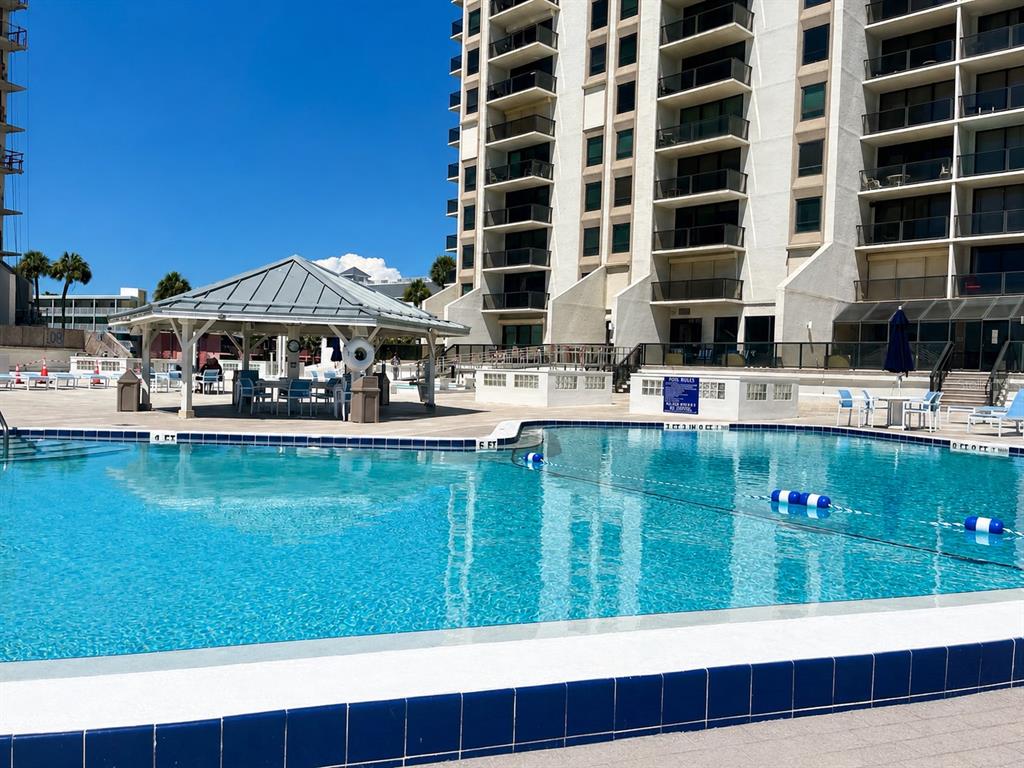 A swimming pool sits in front of a multi-story building with balconies and a gazebo — 450 S GULFVIEW BOULEVARD UNIT 708, CLEARWATER BEACH, FL