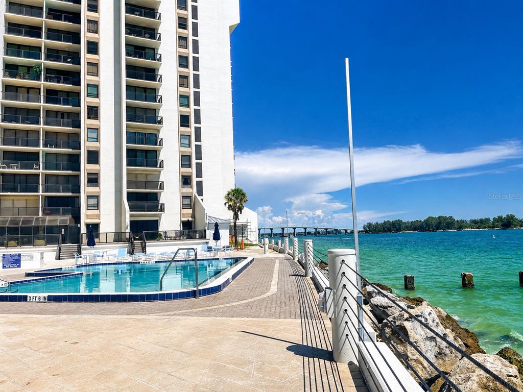 A swimming pool sits on a patio next to a high-rise building and the ocean — 450 S GULFVIEW BOULEVARD UNIT 708, CLEARWATER BEACH, FL