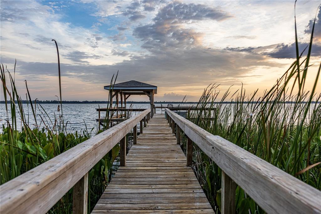 A wooden pier with a covered boat dock extends into a lake at sunset — 32834 LAKESHORE DRIVE, TAVARES, FL