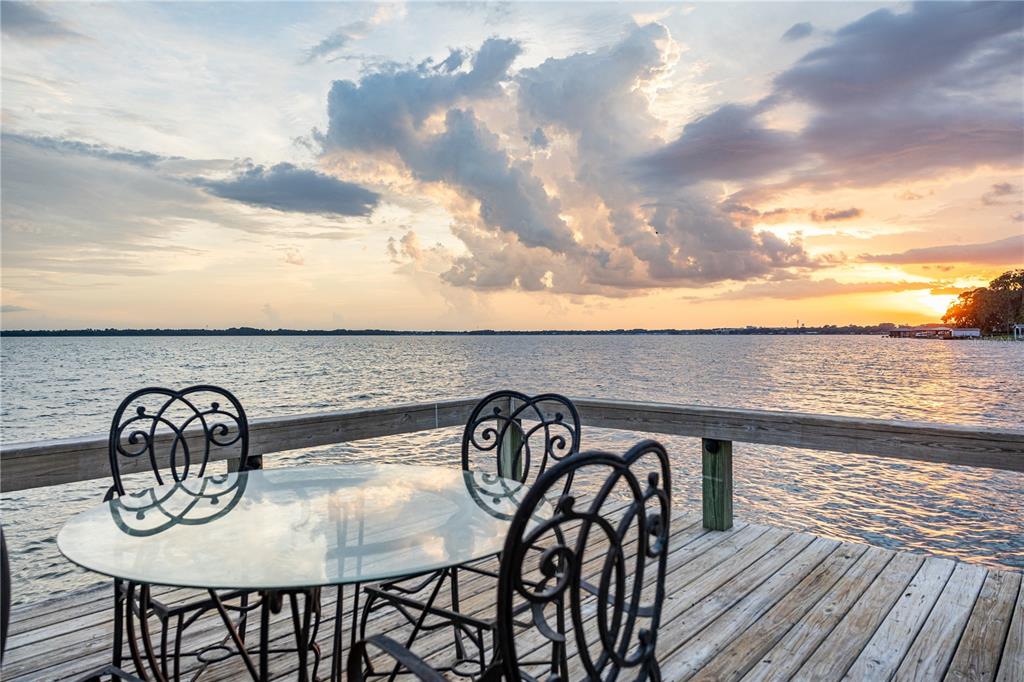 A glass-topped table and metal chairs sit on a wooden deck overlooking a lake — 32834 LAKESHORE DRIVE, TAVARES, FL