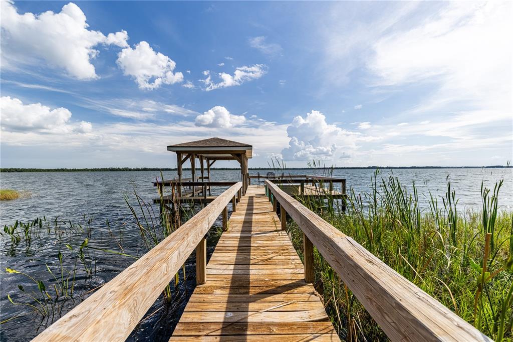 A wooden pier with a covered gazebo extends over a lake under a cloudy sky — 32834 LAKESHORE DRIVE, TAVARES, FL