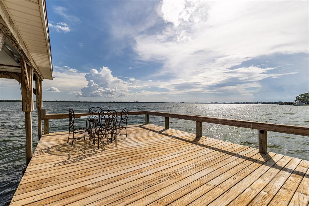 A wooden dock with a patio table and chairs overlooks a large lake — 32834 LAKESHORE DRIVE, TAVARES, FL