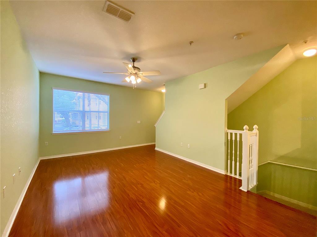 An empty living room features light green walls, hardwood flooring, and a white staircase railing — 1608 LEGACY PARK DRIVE UNIT 1608, MAITLAND, FL