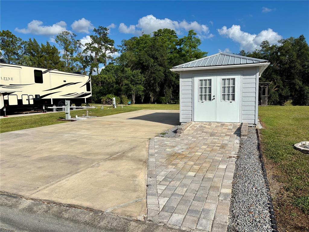 A small shed with double doors sits next to a concrete pad and paver walkway — 2929 NE 101ST TERRACE, SILVER SPRINGS, FL