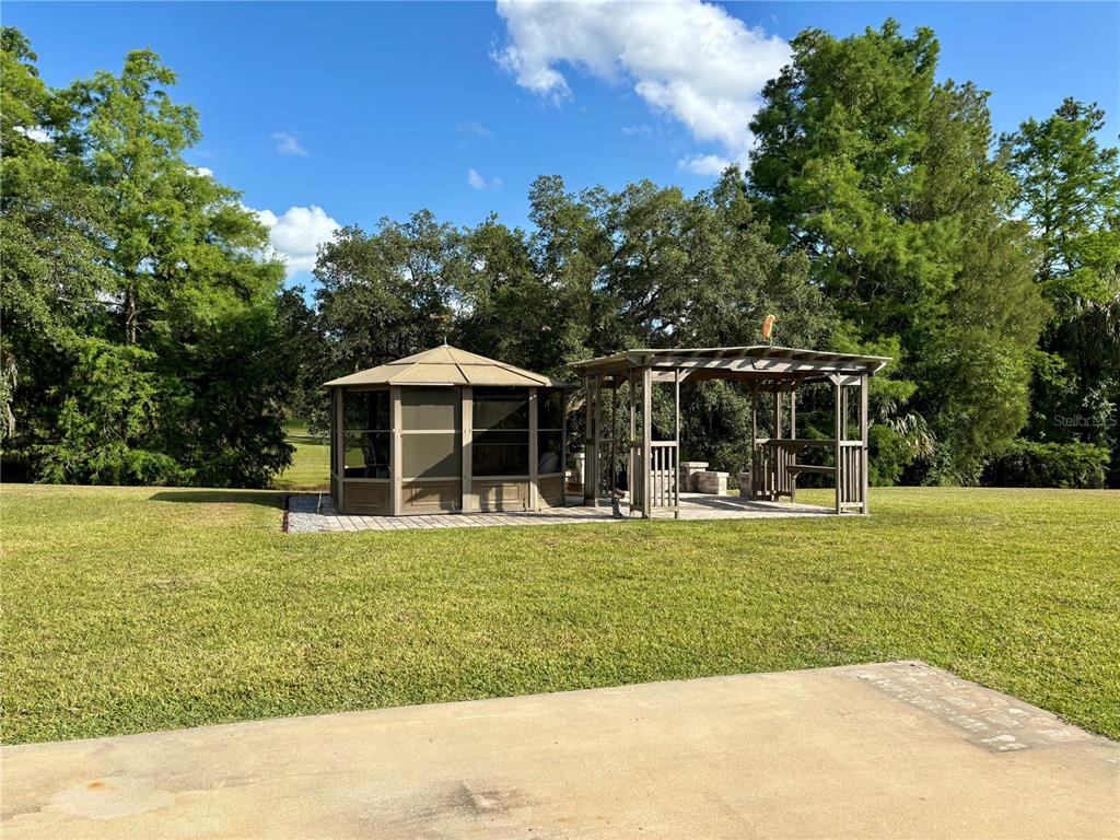 A backyard features a screened gazebo and an adjacent wooden pergola on a paved patio — 2929 NE 101ST TERRACE, SILVER SPRINGS, FL
