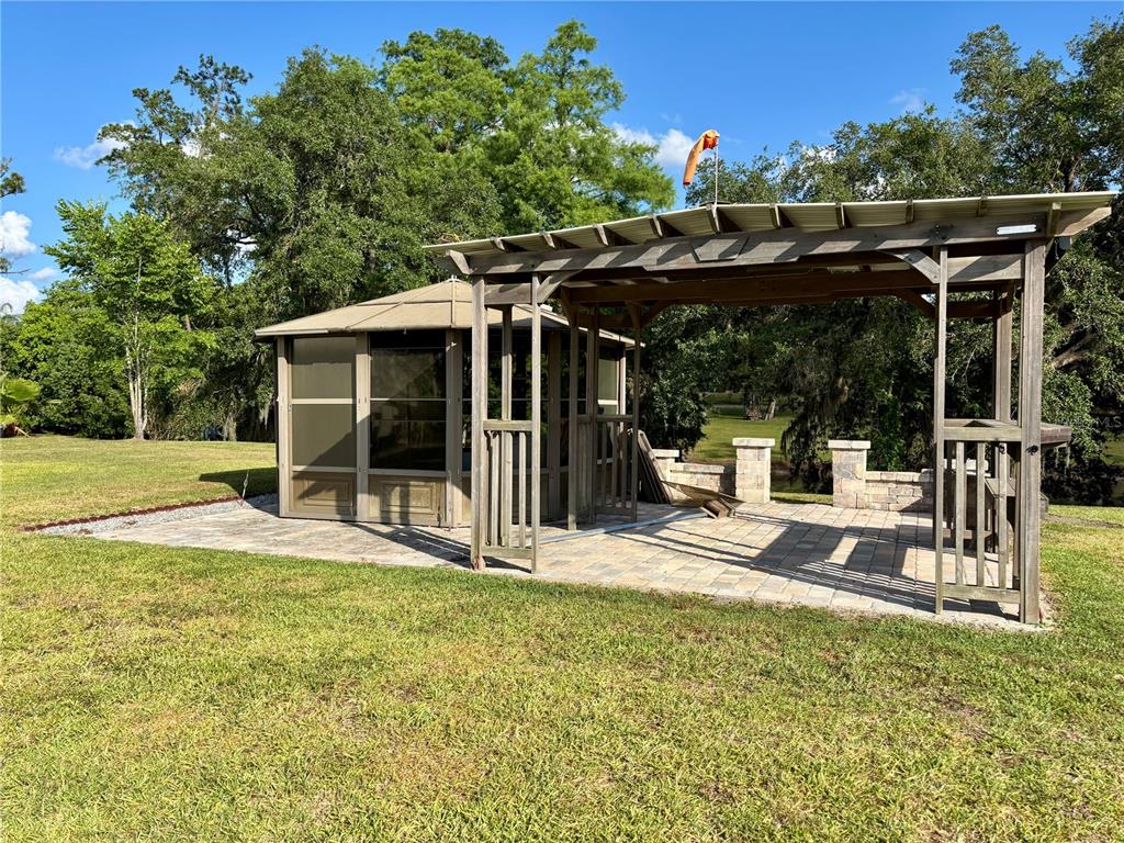 A backyard patio features a screened gazebo and a wooden pergola over stone pavers — 2929 NE 101ST TERRACE, SILVER SPRINGS, FL