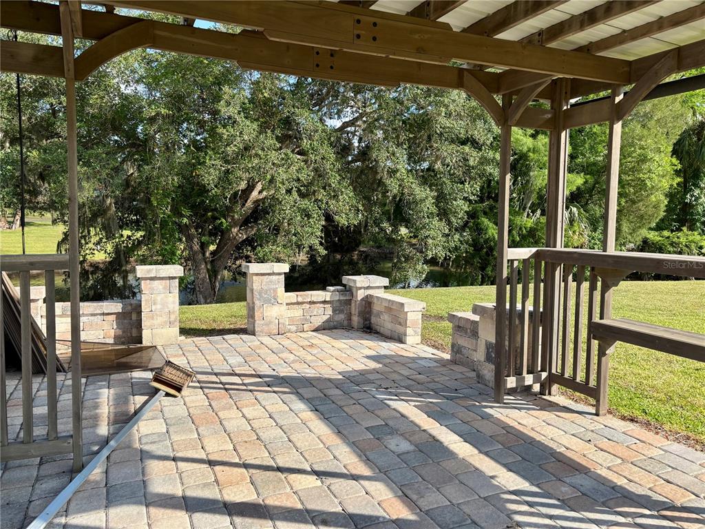 A covered stone patio features a wooden pergola, built-in seating, and views of a pond — 2929 NE 101ST TERRACE, SILVER SPRINGS, FL