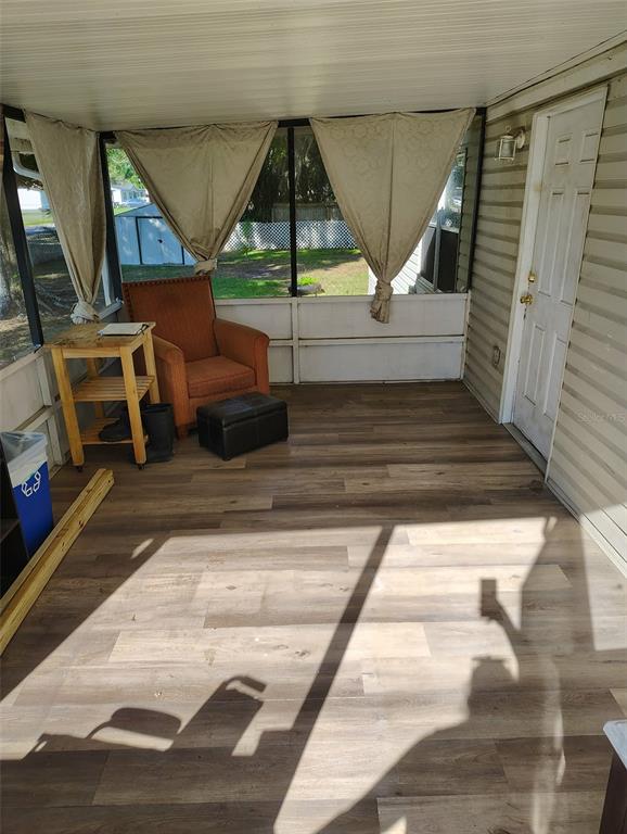 A screened-in porch with wood-look flooring, an orange armchair, and a small wooden side table — 2974 BRENDA LANE, AUBURNDALE, FL