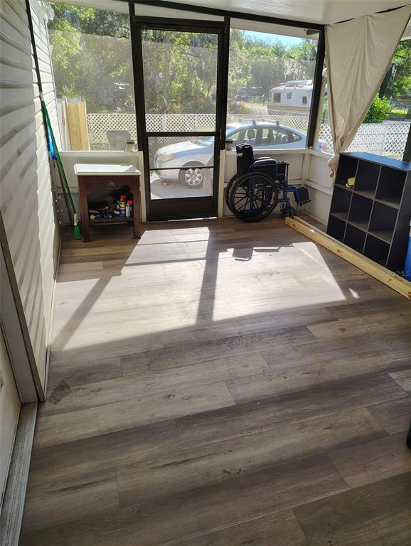 A screened-in porch with wood-look flooring, a wheelchair, a small table, and shelving units — 2974 BRENDA LANE, AUBURNDALE, FL