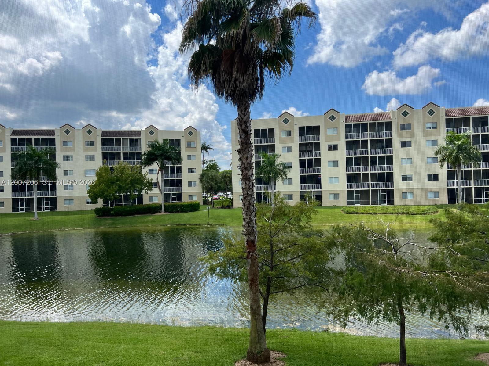 A view of a pond and palm trees in front of two multi-story apartment buildings — 10720 NW 66th St # 206, Doral FL 33178, DORAL, FL