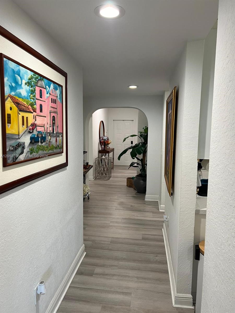 A hallway with light wood-look flooring leads to an arched entryway and a front door — 10720 NW 66th St # 206, Doral FL 33178, DORAL, FL