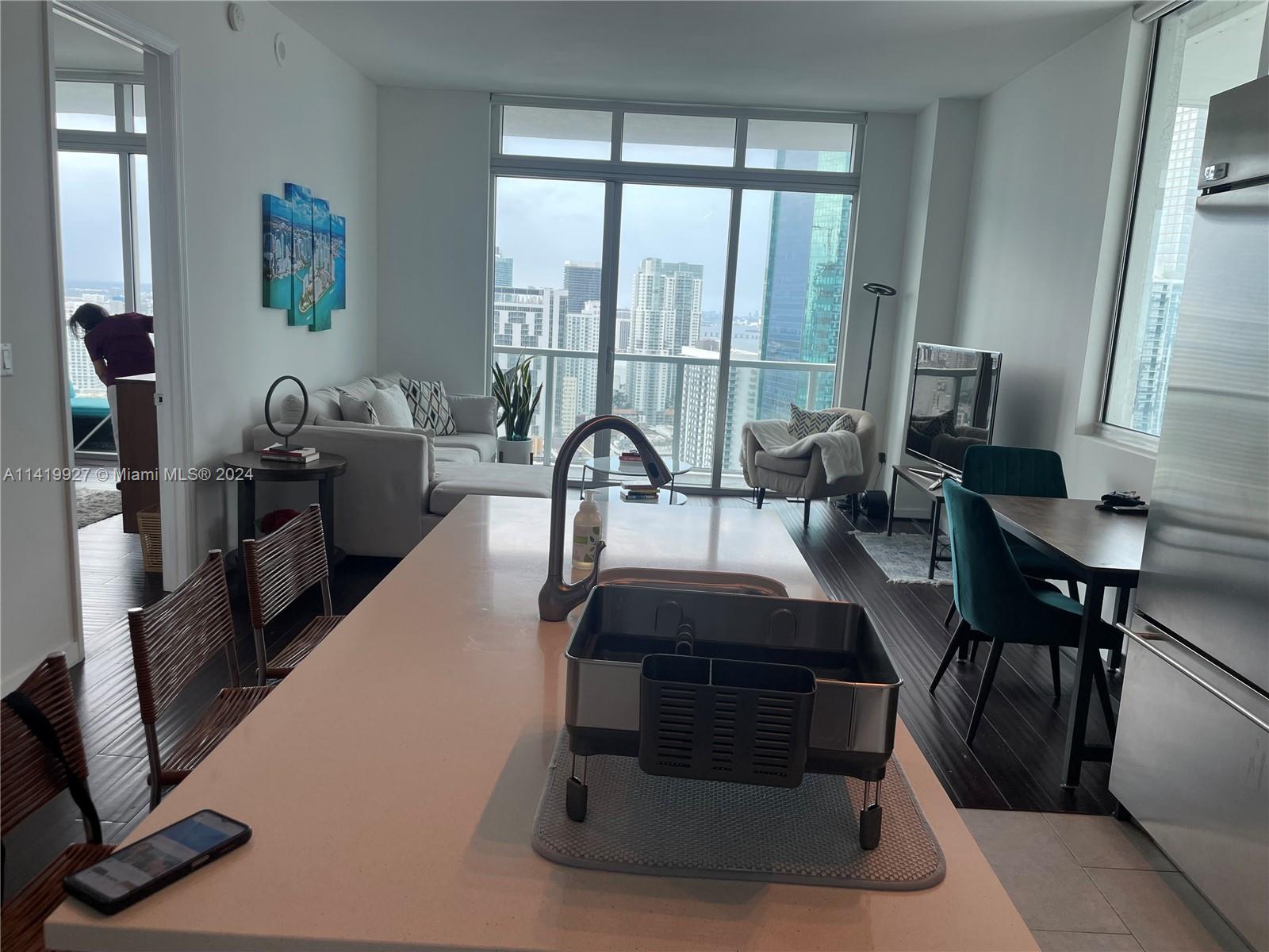 A kitchen island with a dish rack overlooks a living area with floor-to-ceiling city views — 55 SE 6th St, Miami FL 33131, MIAMI, FL