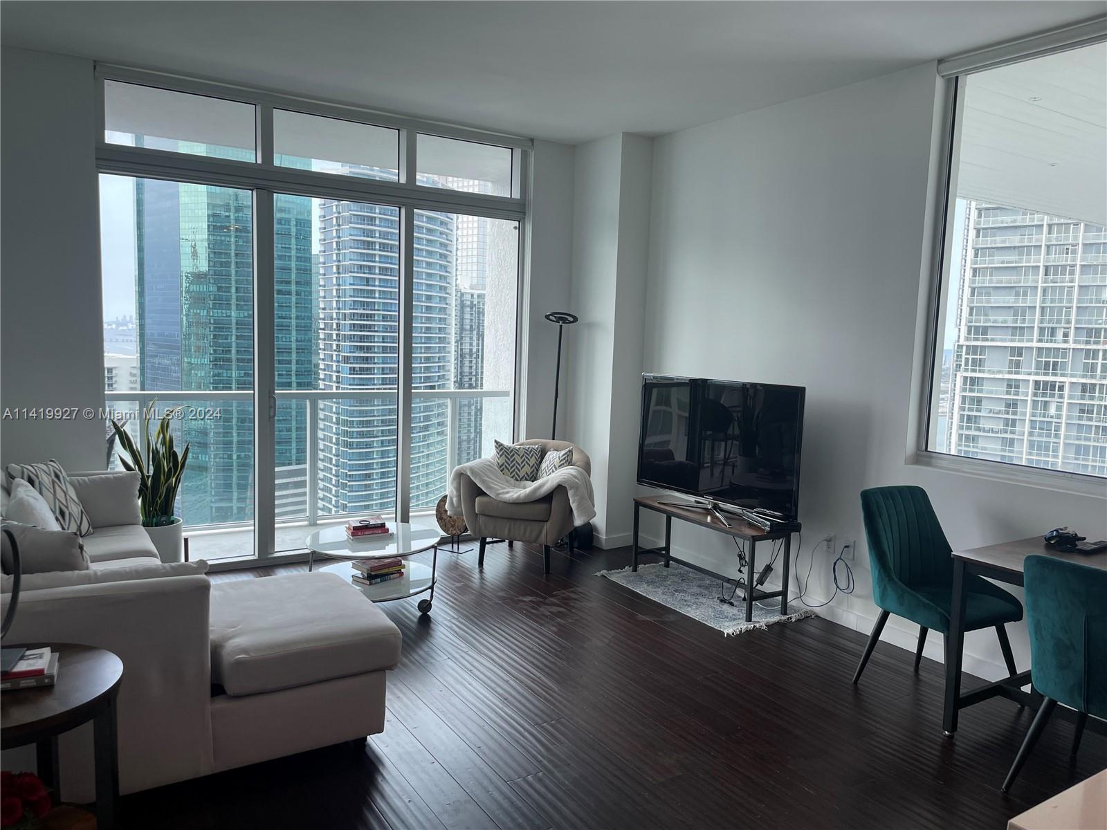 A living room with dark wood floors, a sectional sofa, and floor-to-ceiling windows overlooking skyscrapers — 55 SE 6th St, Miami FL 33131, MIAMI, FL