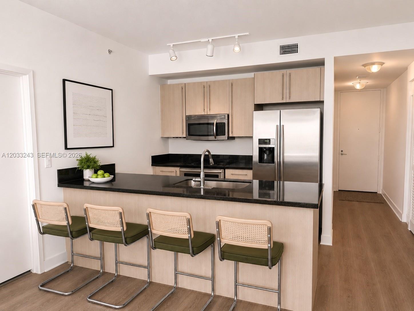 A kitchen features light wood cabinets, black countertops, stainless steel appliances, and four bar stools — MIAMI, FL