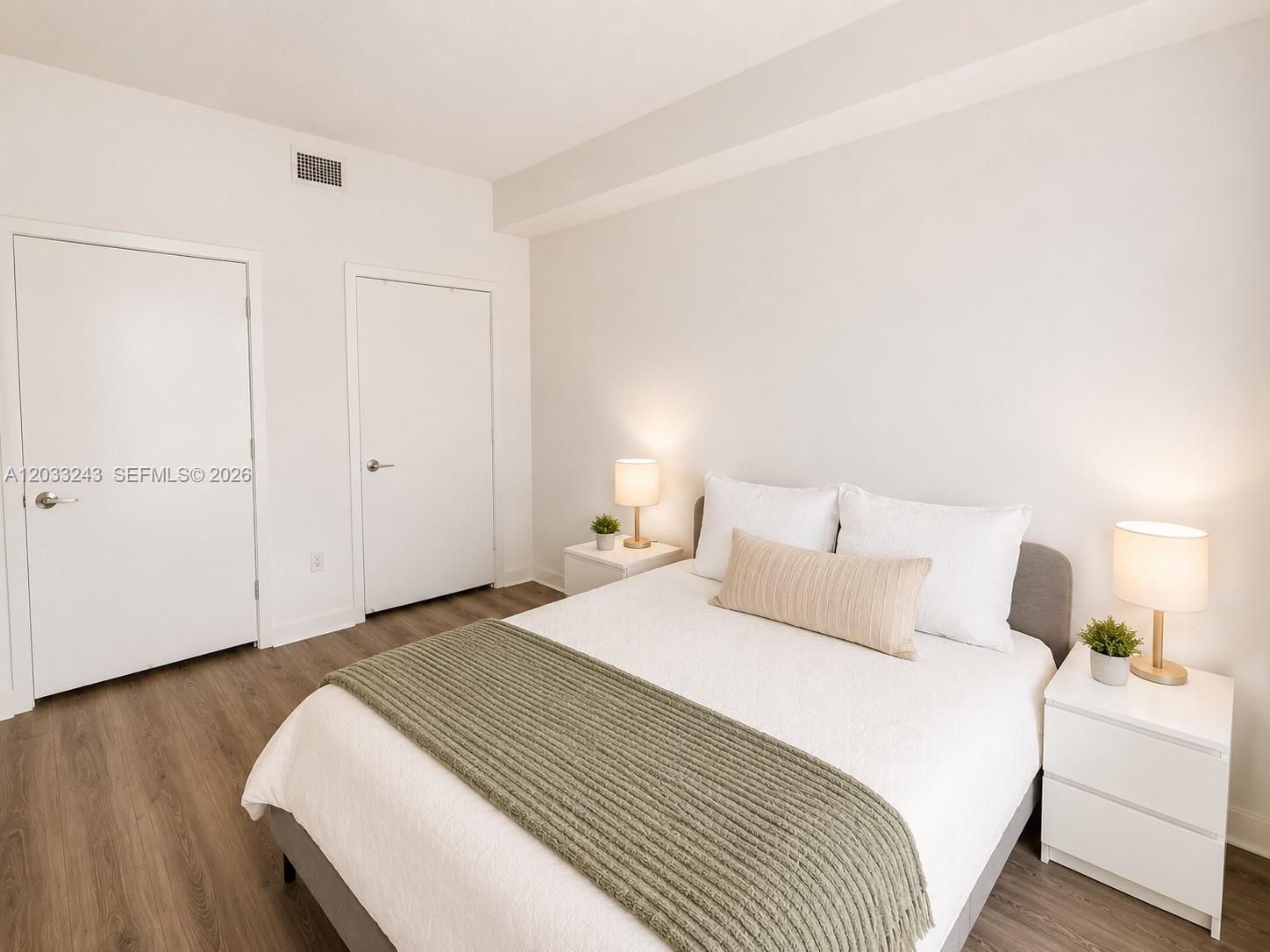 A bedroom features a bed with white bedding, a green throw, and two white nightstands — MIAMI, FL