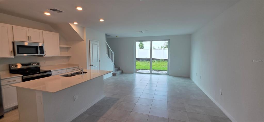 A kitchen with white cabinets and a quartz island opens to a tiled living area — 14523 LILAC SKY TERRACE, BRADENTON, FL