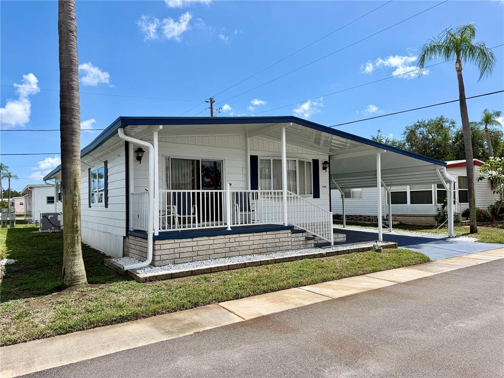 A white mobile home features a front porch, a carport, and a brick-patterned foundation — 34548 VIOLET DRIVE N, PINELLAS PARK, FL