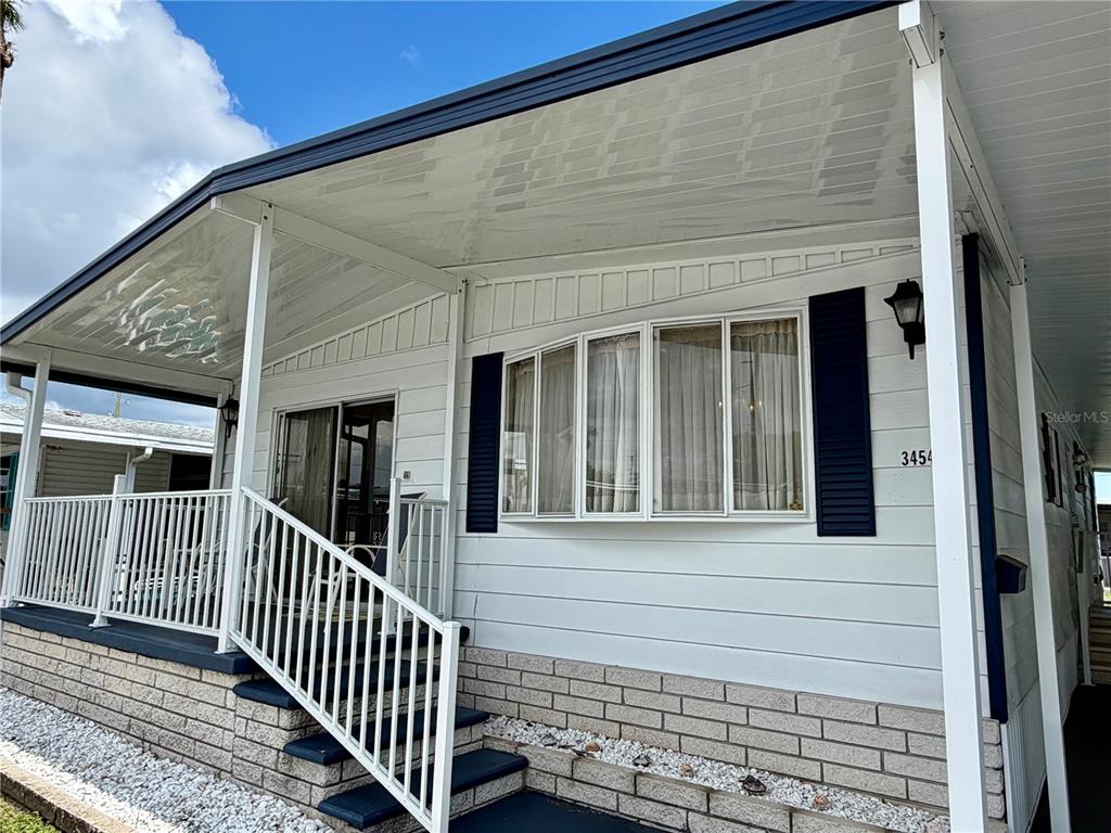 A white mobile home exterior features a covered porch, white railings, and a bay window — 34548 VIOLET DRIVE N, PINELLAS PARK, FL